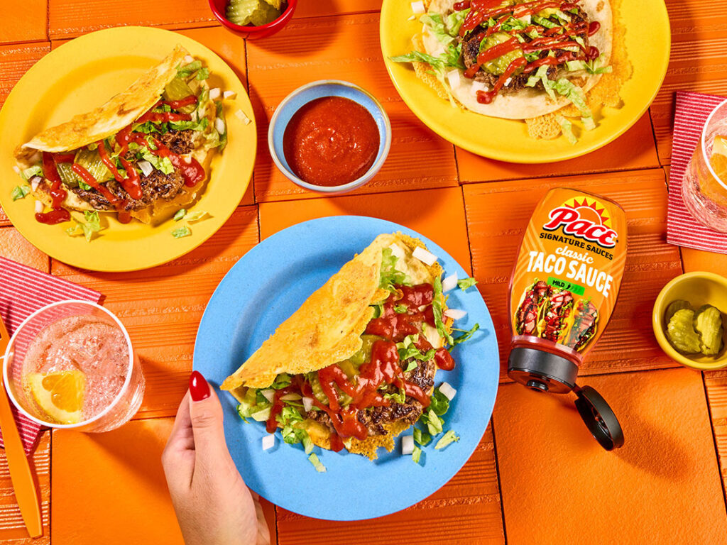 An image of prepared Cheesy Smashburger Tacos made with ground beef, Pace® Signature Sauces Classic Taco Sauce, Cheddar cheese, flour tortillas, iceberg lettuce, dill pickle and onion.
