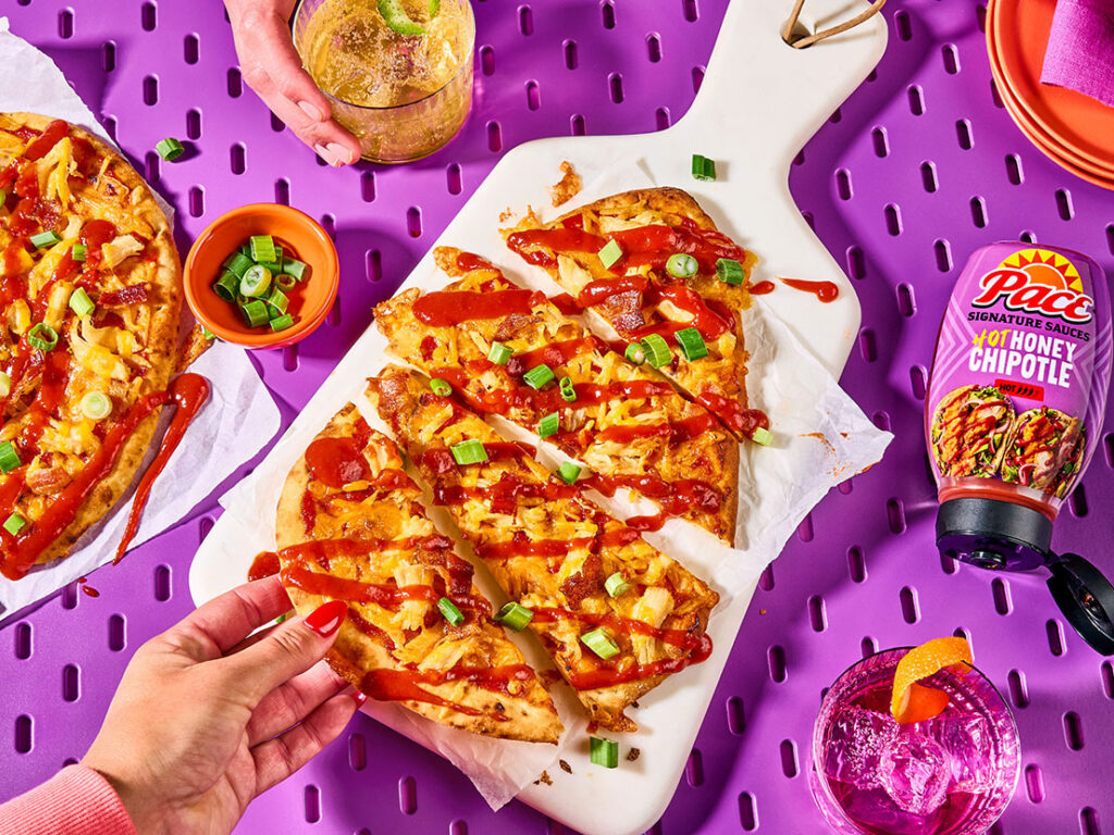 An image of prepared Hot Honey Chipotle Chicken & Bacon Flatbreads made with naan, Pace® Signature Sauces Hot Honey Chipotle Sauce, rotisserie chicken, Cheddar cheese, bacon, green onion and blue cheese.