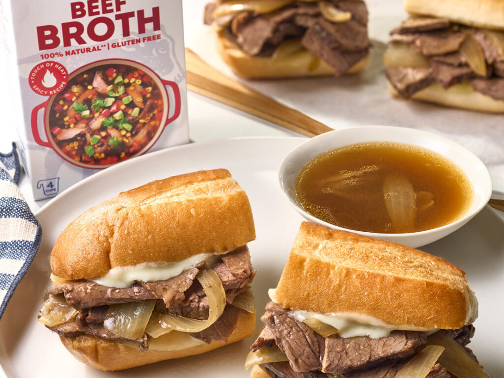 An image of prepared Spicy Slow Cooker French Dip Sandwiches with Provolone made with beef, onions, Swanson® Spicy Beef Broth, hoagie rolls and provolone cheese.
