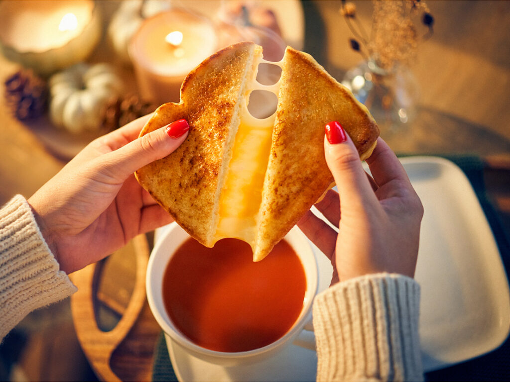 Image of Tomato Soup & Grilled Cheese with a person pulled grilled cheese apart